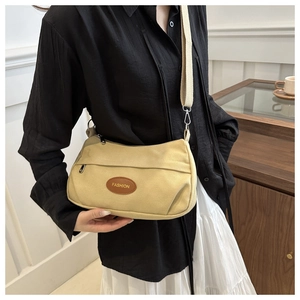Detail of beige canvas crossbody bag featuring adjustable wide strap and brown fashion patch