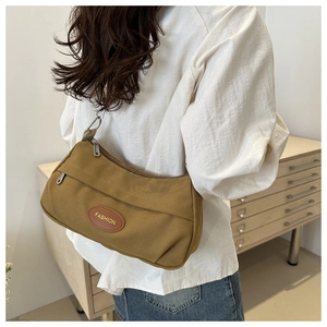 Detail of ochre canvas shoulder bag with leather patch and zipper on minimalist background