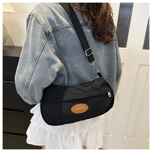 Detail of black canvas half-moon bag with adjustable wide strap and brown fashion label