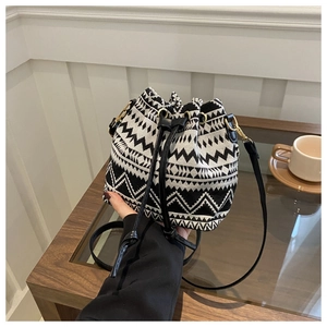 Close-up of hand-held geometric woven bucket bag with black leather drawstring and strap
