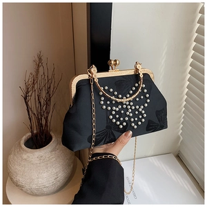 Close-up of black silk evening bag with pearl butterfly and golden metal chain