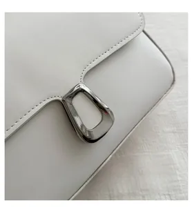Macro shot of white leather texture and silver geometric buckle on crossbody bag
