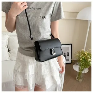 Minimalist black matte leather crossbody bag with silver buckle worn by a model