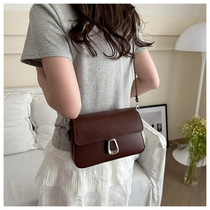 Detail view of dark brown faux leather crossbody bag with silver magnetic buckle on a model