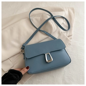 Detailed close-up of a dusty blue crossbody bag with a silver trapezoidal lock on a blazer