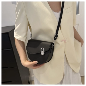 Detail of a matte black saddle bag with silver oval metal buckle on a beige blazer