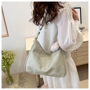Détail du sac hobo vert clair avec breloque pompon rose et texture cuir PU souple