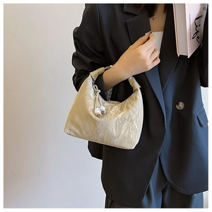 Detail of beige wrinkled texture hobo bag with white bead charms on a model in black suit