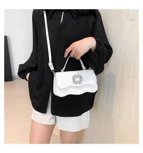 Close-up of white wave-textured bag featuring a crystal buckle and adjustable strap