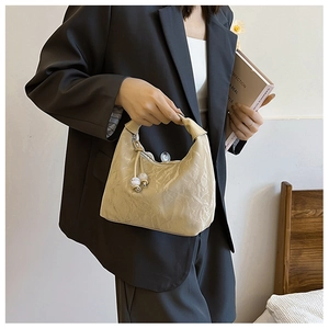 Detail of beige pleated shoulder bag with pearl pendant and wide handle on a model