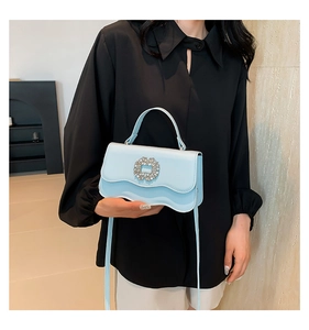Detail of light blue handbag with wave edge design and rhinestone buckle in hand