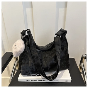 Détail du sac fourre-tout noir texturé avec breloque cœur en peluche blanche sur un livre