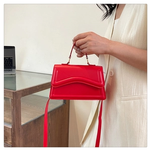 Detail of red leather handbag showing wave-stitched flap and elegant top handle