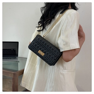 Détail d'un sac bandoulière matelassé noir avec chaîne dorée et fermoir rotatif