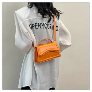 Sac bandoulière orange vif tendance porté par un mannequin sur un fond gris épuré