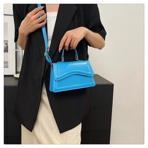 Detail of bright blue crossbody bag with wave flap design and matte leather texture