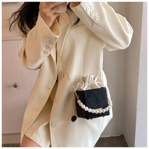 Close-up of black textured bucket bag with pearl handle and gold chain strap on model
