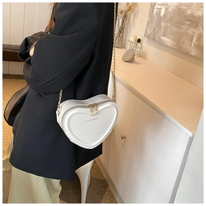 Weiße herzförmige Umhängetasche mit goldener Kette an einem Modell für den Alltag