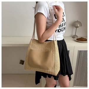 Detail of woven straw tote bag featuring a brown faux leather pocket and cotton rope handles