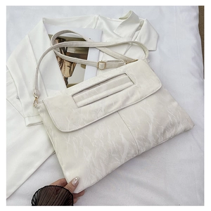 Détail du sac blanc texturé avec poignée creuse et boucle dorée sur fond minimaliste