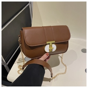 Detail of a brown crossbody bag featuring a gold chain strap and elegant T-shaped metal lock