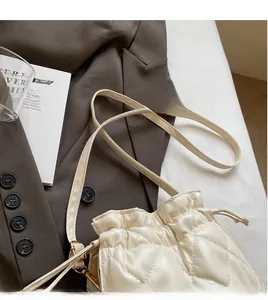 Detail of cream white quilted PU leather crossbody bag with drawstring on brown blazer