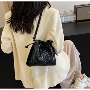 Detail of black quilted leather bucket bag with drawstring closure and golden buckle