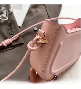 Close-up of pink leather crossbody bag with polished gold ring hardware and knot detail