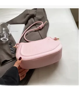 Detail of pink half-moon shoulder bag with knotted strap on grey blazer with magazine
