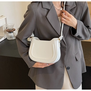 Detail of white saddle bag with U-shaped embossing and woven shoulder strap on model