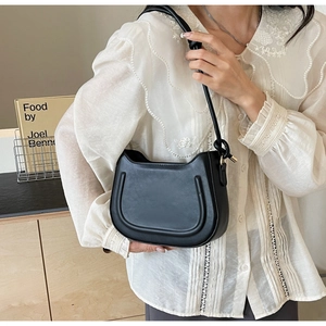 Side view of black leather saddle bag featuring unique knot strap and golden hardware details