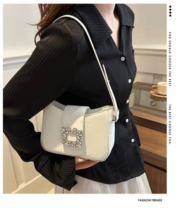 Close-up of white underarm bag featuring a square rhinestone buckle and smooth leather