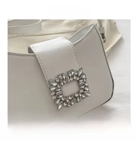 Detailed close-up of a white leather baguette bag with a crystal-encrusted square buckle