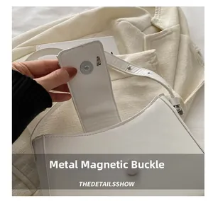 Close-up of the white leather handbag featuring a silver cylindrical magnetic snap closure