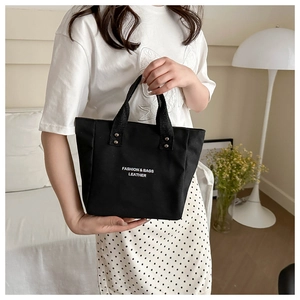 Vue détaillée du sac cabas en toile noire avec lettrage mode et rivets métalliques