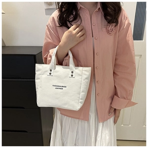 Close-up of white canvas bucket bag with fashion lettering and rivet detail on handle