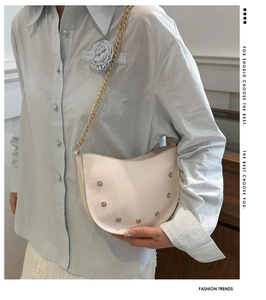 Close-up of white semi-circular shoulder bag with crystal rivets and gold chain strap