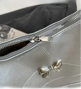 Close-up of smooth metal zipper and silver bow detail on the textured tote bag