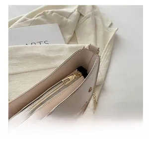 Close-up of smooth gold zipper and metallic chain on a cream PU leather saddle bag