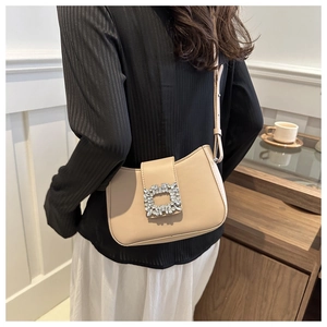 Close-up of cream leather baguette bag with a crystal buckle on a model's shoulder