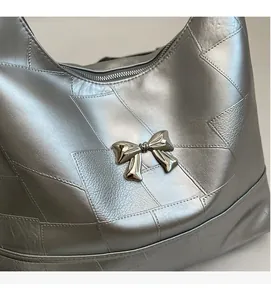 Macro detail of metallic silver bucket bag with bow ornament and geometric patch stitching