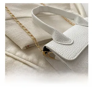 Detailed close-up of textured white leather handbag with golden metal chain hooks