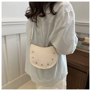 White crescent saddle bag with silver studs and gold chain strap shown on a model