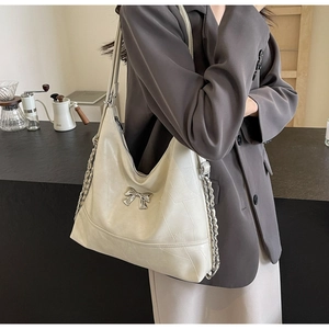 Detail of hobo bucket bag with silver bow ornament and metal chain strap in coffee shop