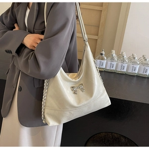 Detail of a beige textured bucket bag with a silver metal bow and chain strap