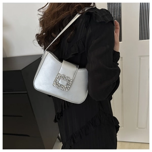 Macro detail of silver shoulder bag featuring a rectangular rhinestone buckle and metallic finish
