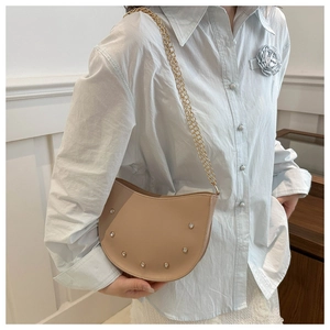 Detail view of beige crescent saddle bag featuring crystal studs and gold chain strap