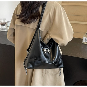 Detail of black bucket bag featuring silver bow accent and adjustable strap worn by model