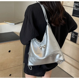 Detail of silver metallic quilted bag featuring a decorative metal bow and chain strap
