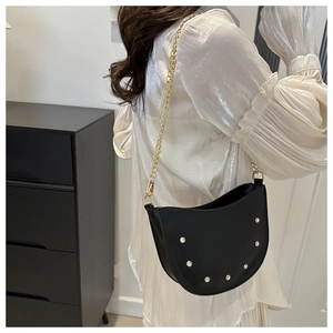 Detail of black half-moon shoulder bag with silver studs and golden chain strap